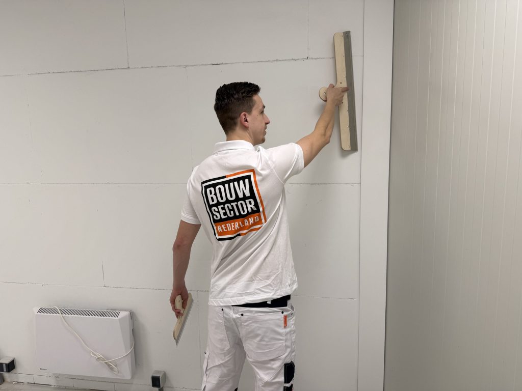 Stukadoor houdt zijn spaan hoog tegen de muur en in de andere hand een kleine plakspaan