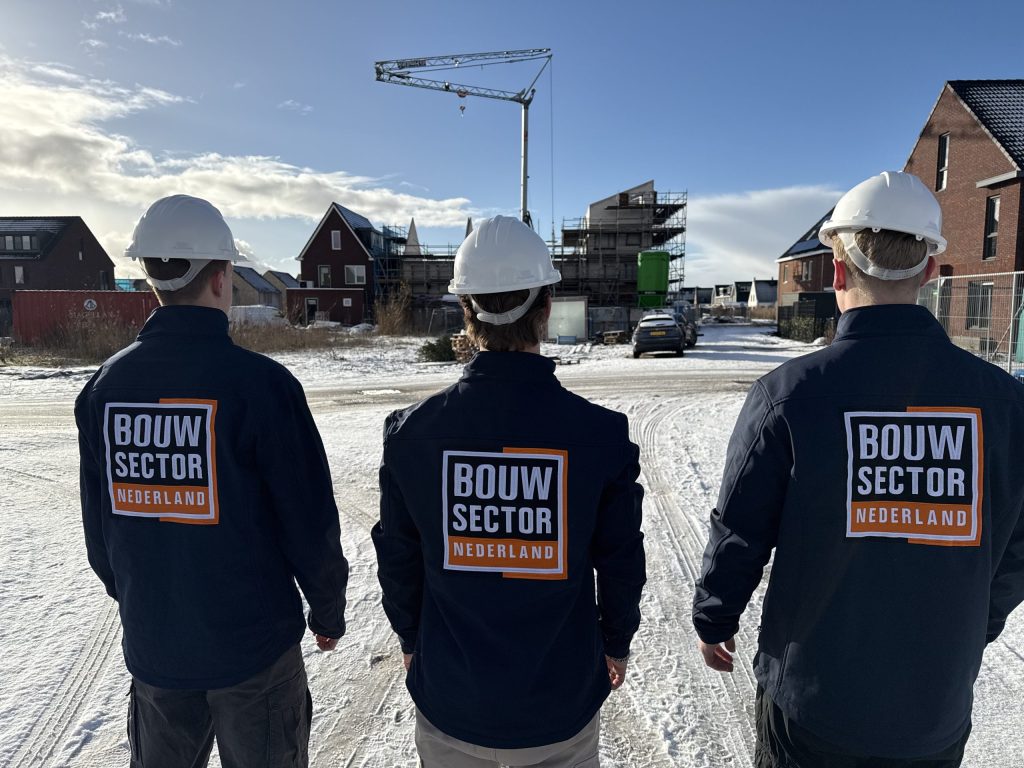 Drie medewerkers van Bouwsector Nederland met bouwhelm op een nieuwbouwlocatie met huizen in aanbouw